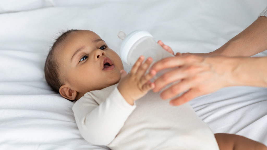 Cute little African American infant drinking from baby bottle