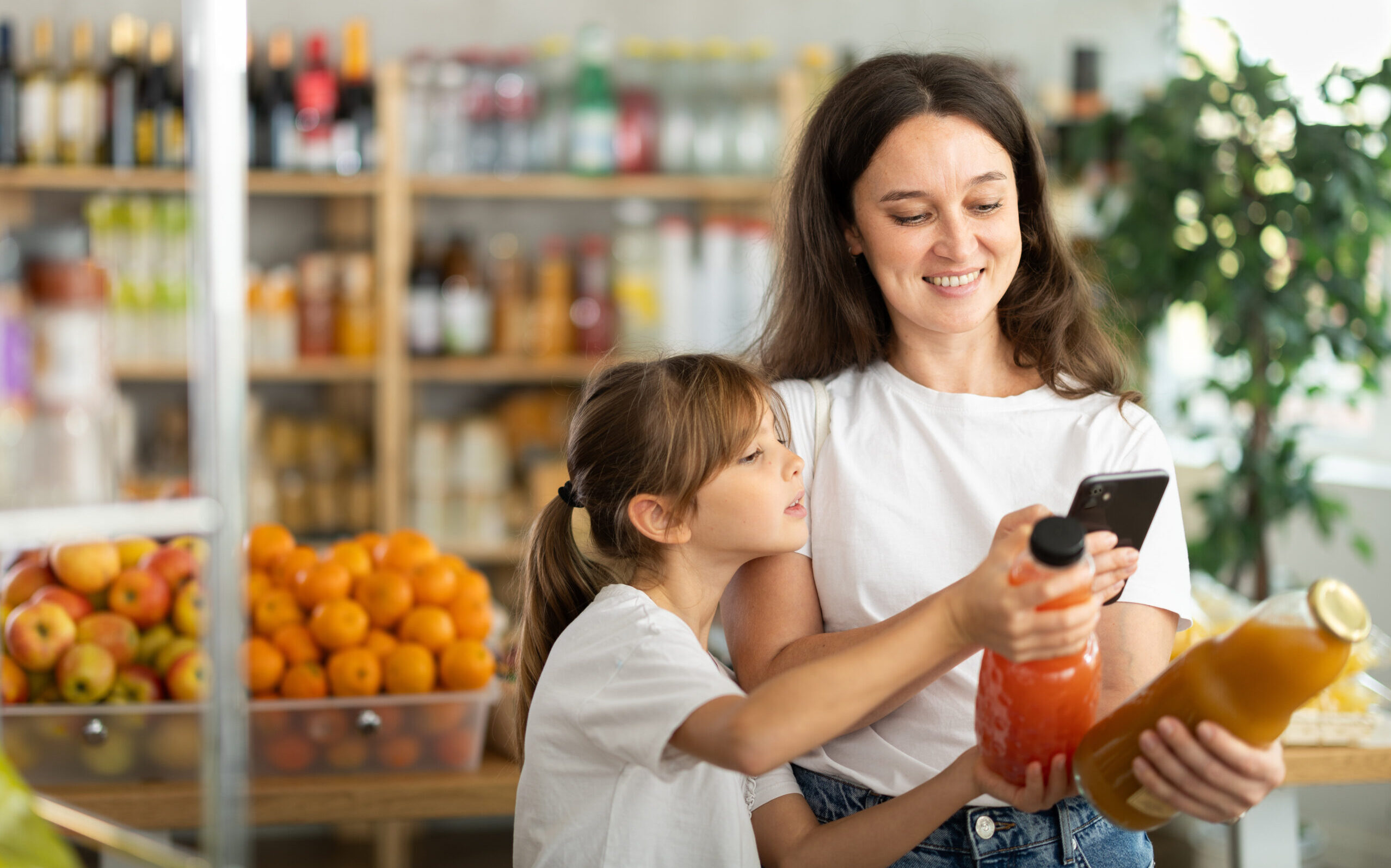 Mother and daughter choose bottles of juice and scan QR code with smartphone